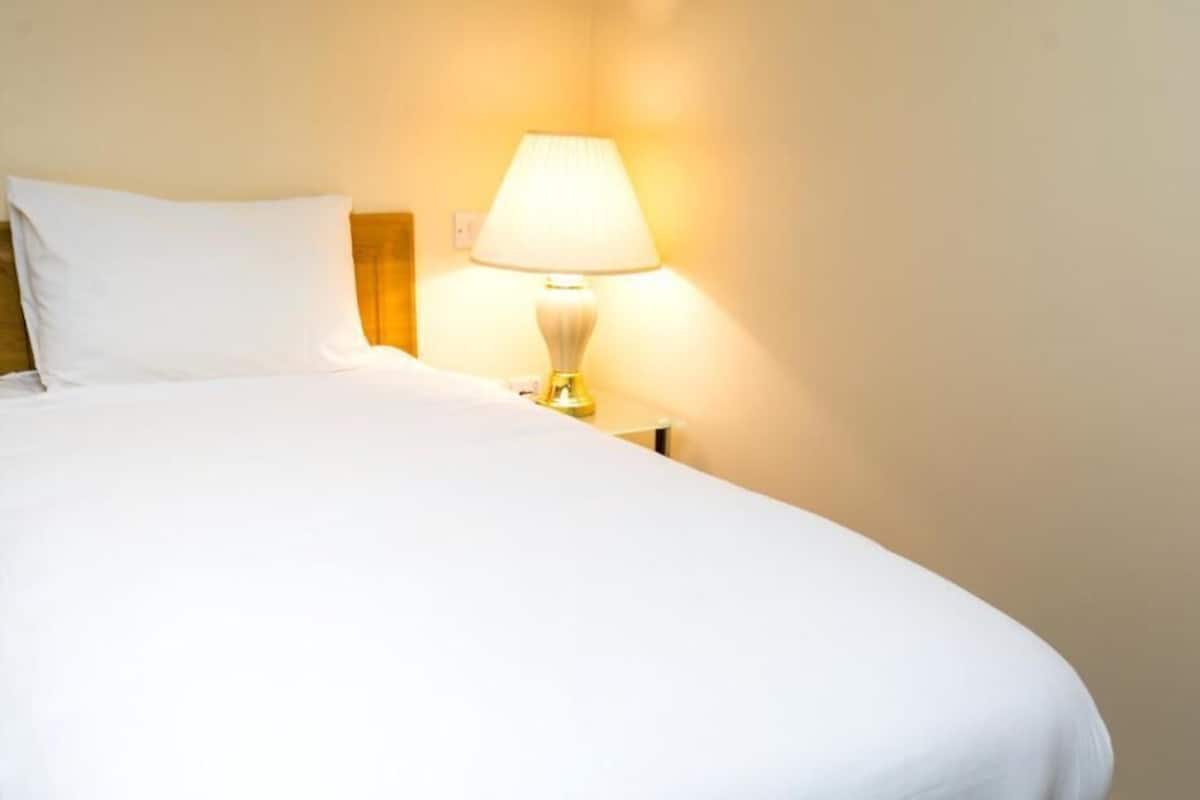 Cama bem arrumada com lençóis brancos e uma luminária de cabeceira.
