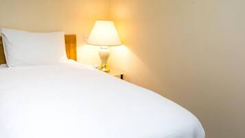 A neatly made bed with white linens and a bedside lamp.