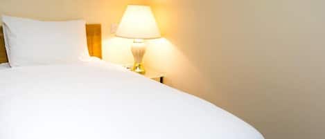 A neatly made bed with white linens and a bedside lamp.
