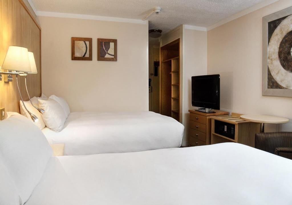 A hotel room with two beds, a TV, a desk with a lamp, and a wardrobe.