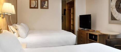 A hotel room with two beds, a TV, a desk with a lamp, and a wardrobe.