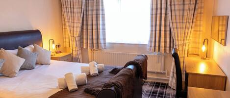 Habitación de hotel con cama, mesita de noche con lámpara, ventana con cortinas y radiador.