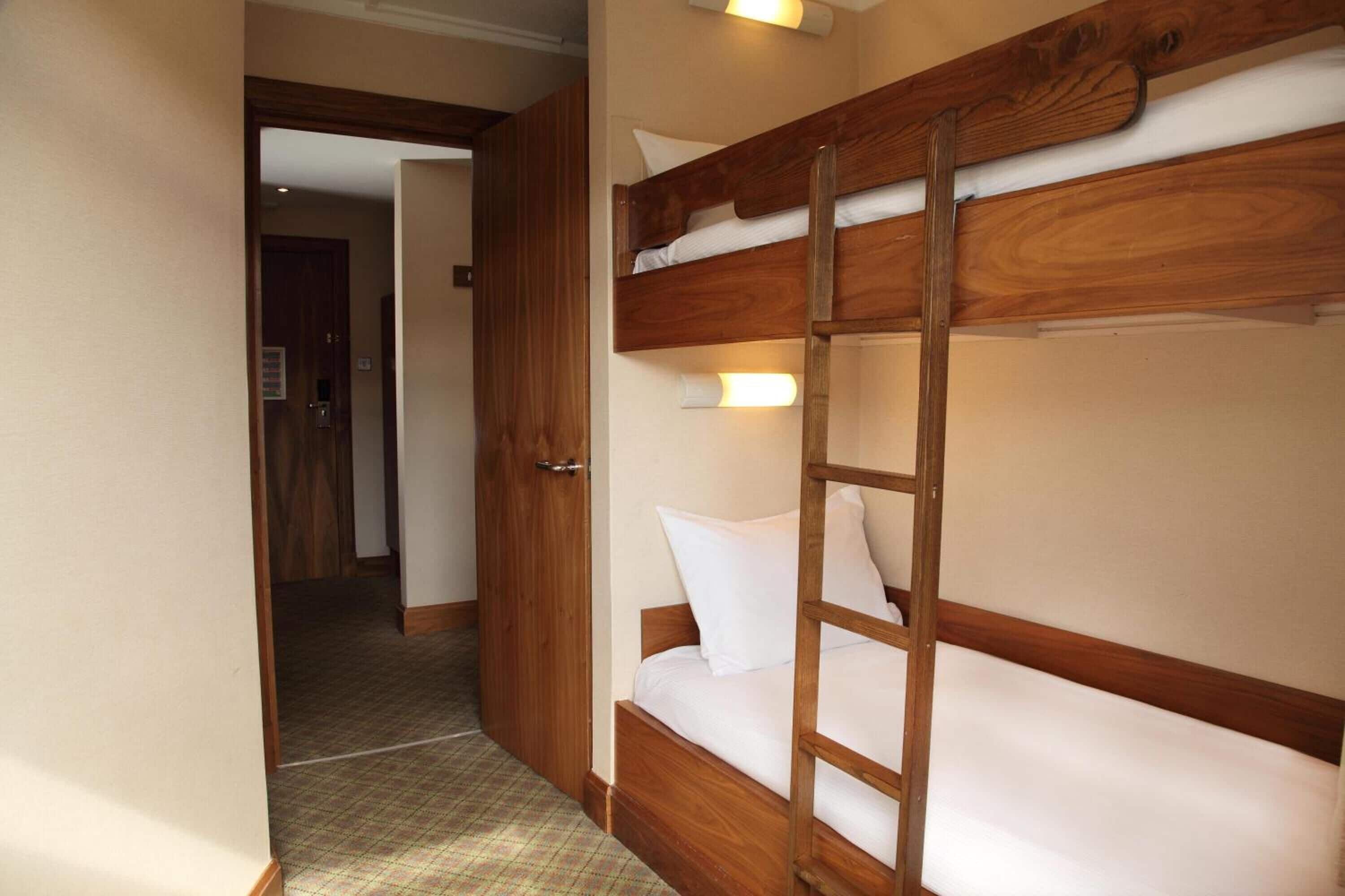 A bunk bed with a wooden frame and a ladder, a door leading to another room, and a patterned floor.