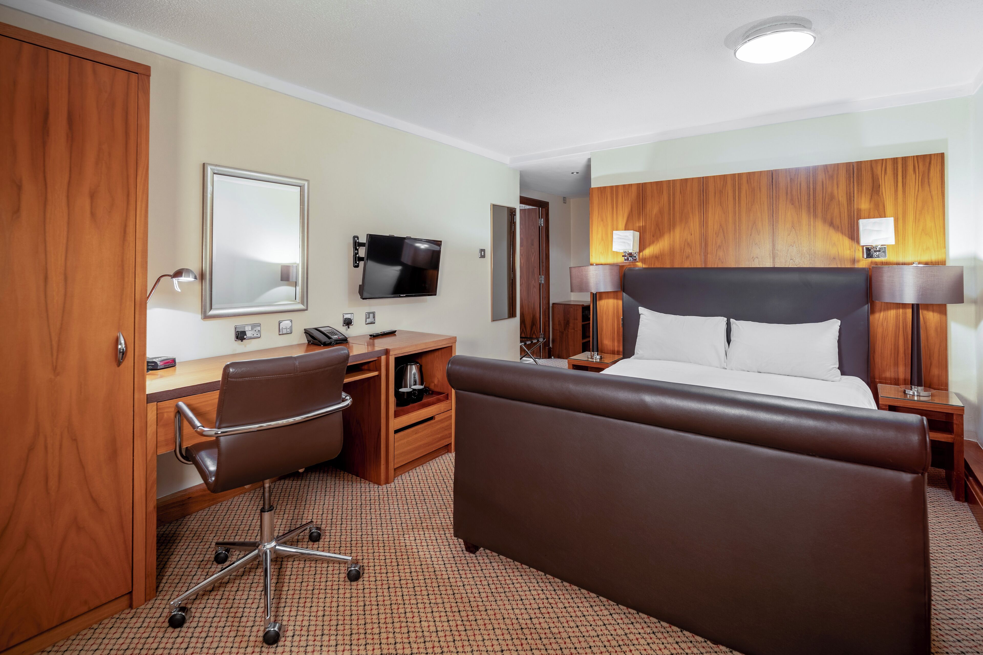 A hotel room with a bed, desk, chair, television, and wooden paneling.