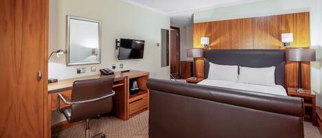 A hotel room with a bed, desk, chair, television, and wooden paneling.