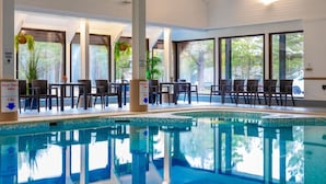 An indoor swimming pool with clear signage indicating a depth of 1-5m, surrounded by lounge chairs and tables, with large windows offering views of the outdoors.