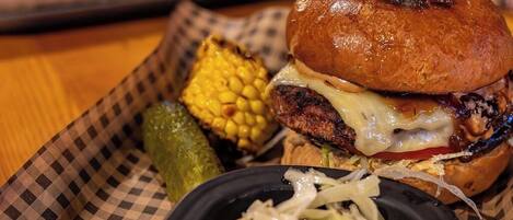 A burger with a toothpick, a side of coleslaw, and a pickle on a checkered paper tray.