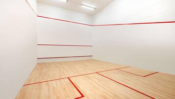 Una cancha de squash con paredes blancas y piso de madera delimitada con líneas rojas.