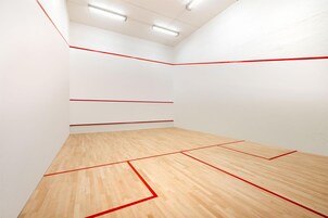 Una cancha de squash con paredes blancas y piso de madera delimitada con líneas rojas.