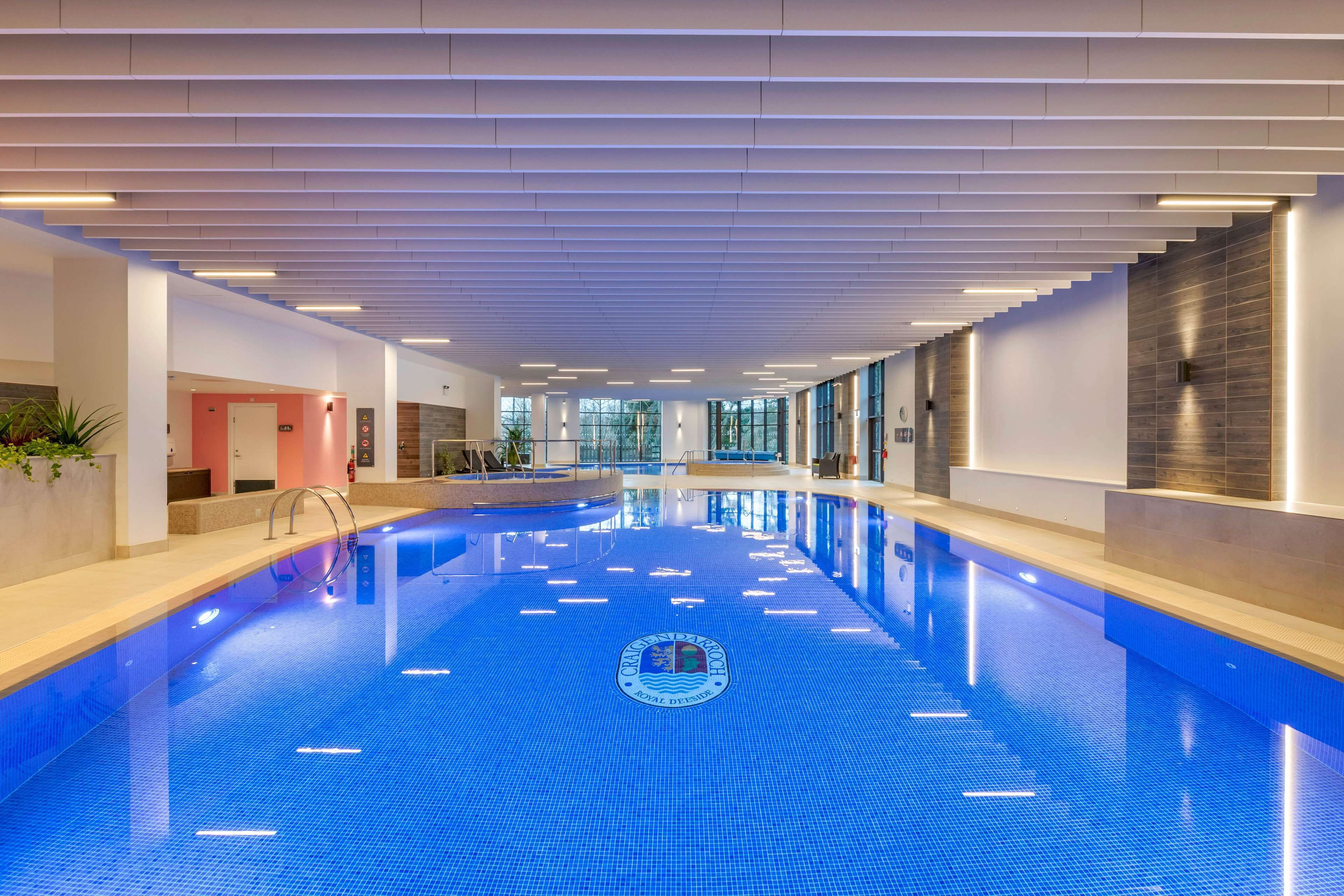 A modern indoor swimming pool with a blue tiled floor and a central logo.