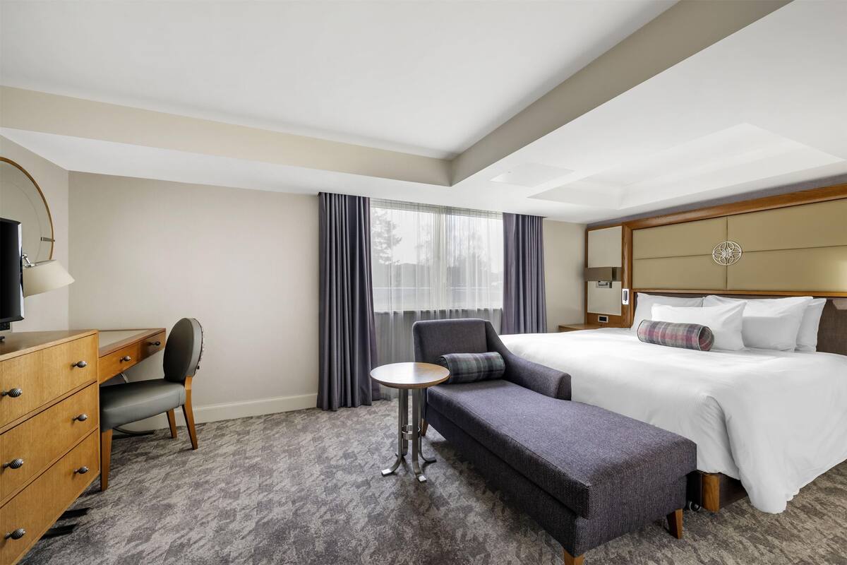 A hotel room with a bed, a desk, a chair, and a small table.