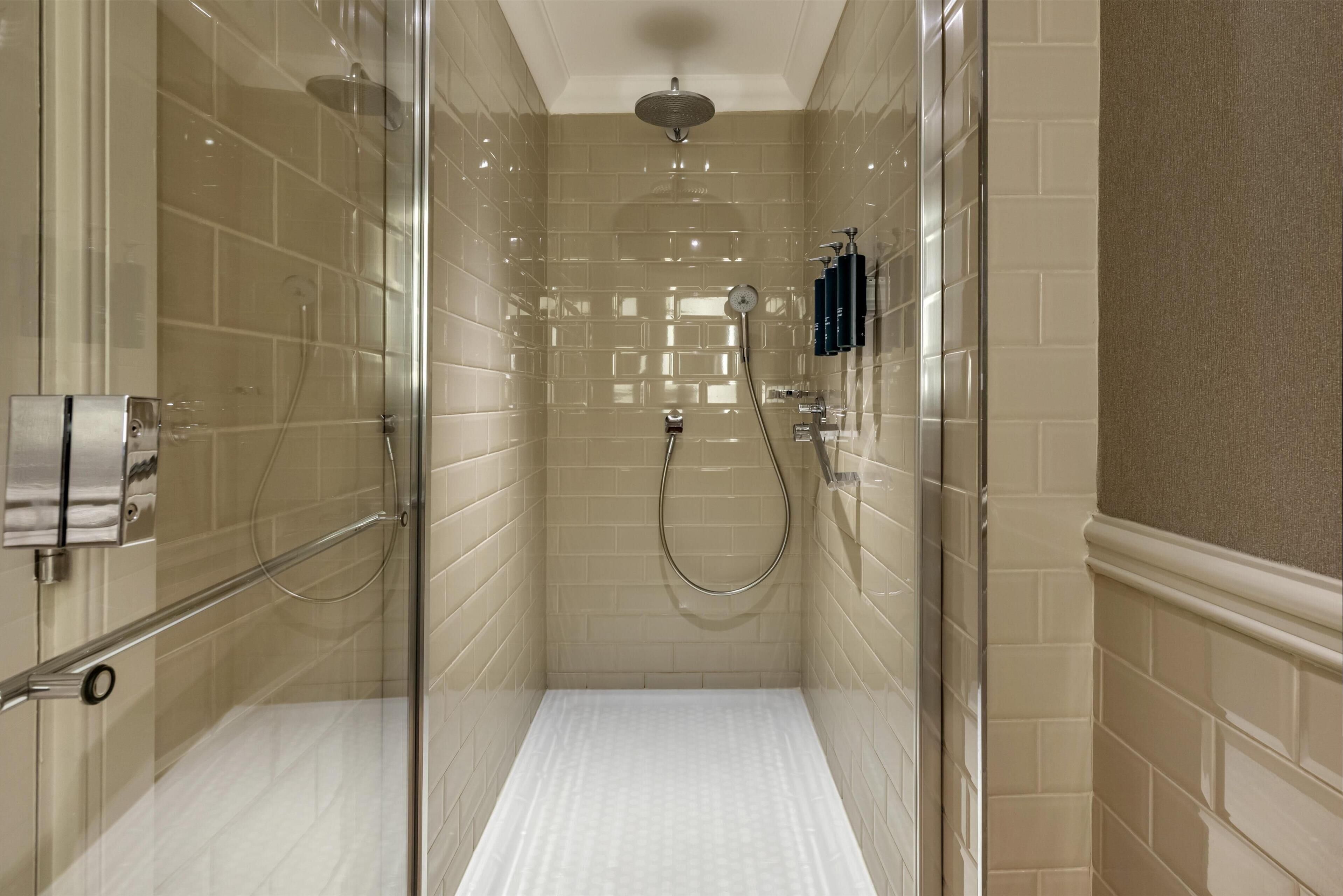 A walk-in shower with beige tiled walls, a glass door, and a handheld showerhead.