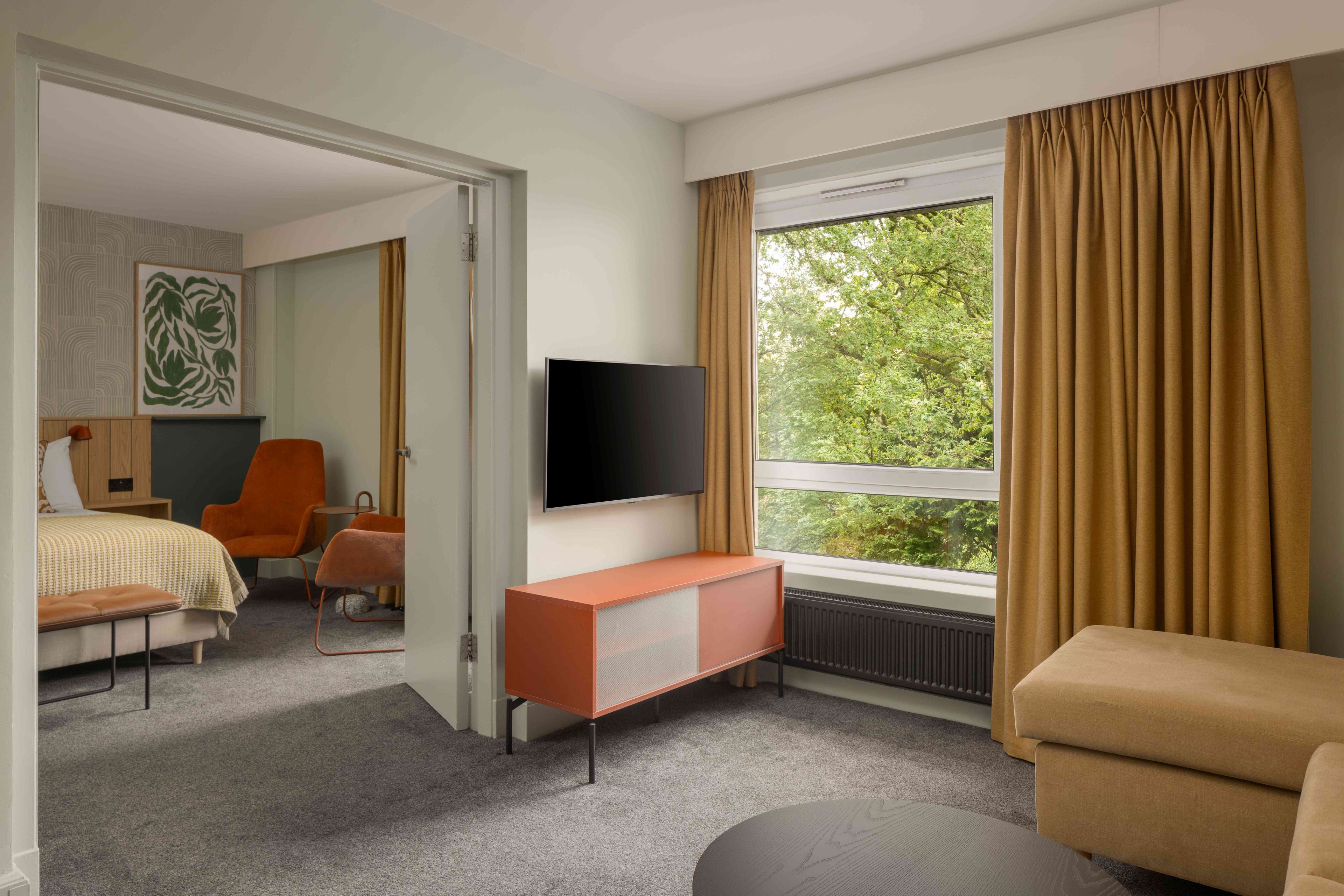 Una habitación de hotel moderna con cama, televisión, sofá y ventana con cortinas.