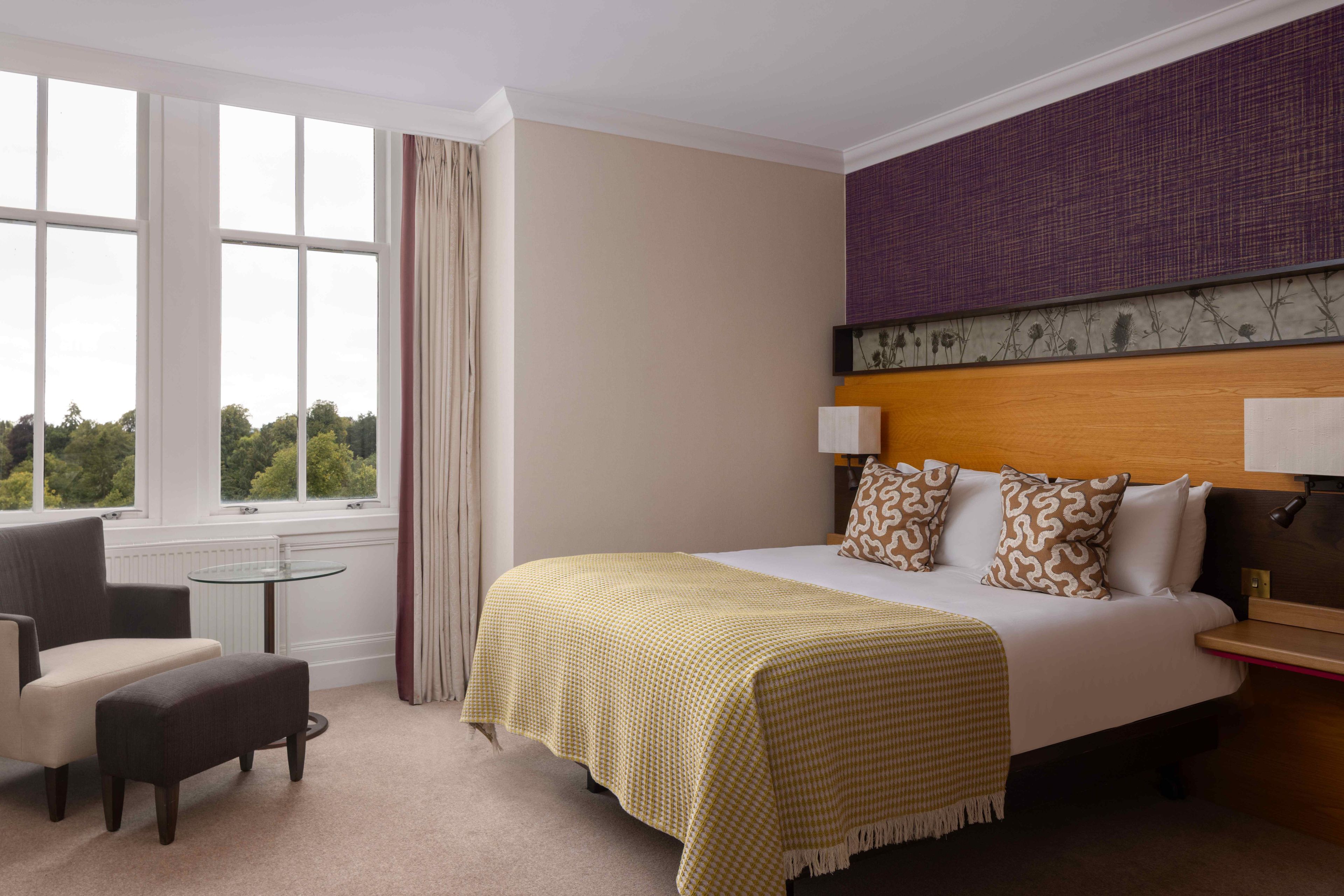A hotel room with a bed, a chair, a small table, and a window with curtains.