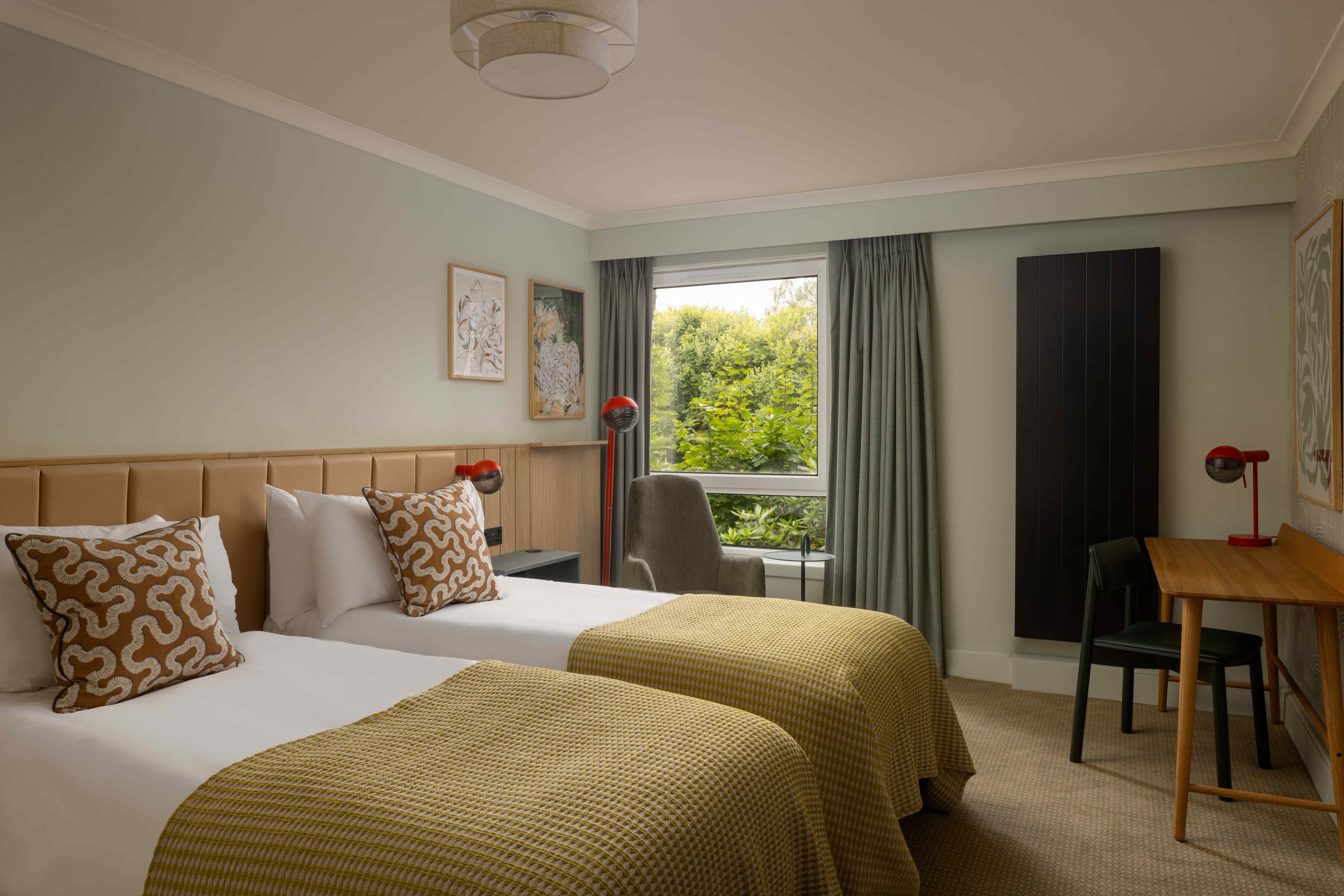 A hotel room with two beds, a desk, a chair, and a window with curtains.
