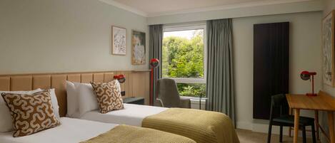 A hotel room with two beds, a desk, a chair, and a window with curtains.