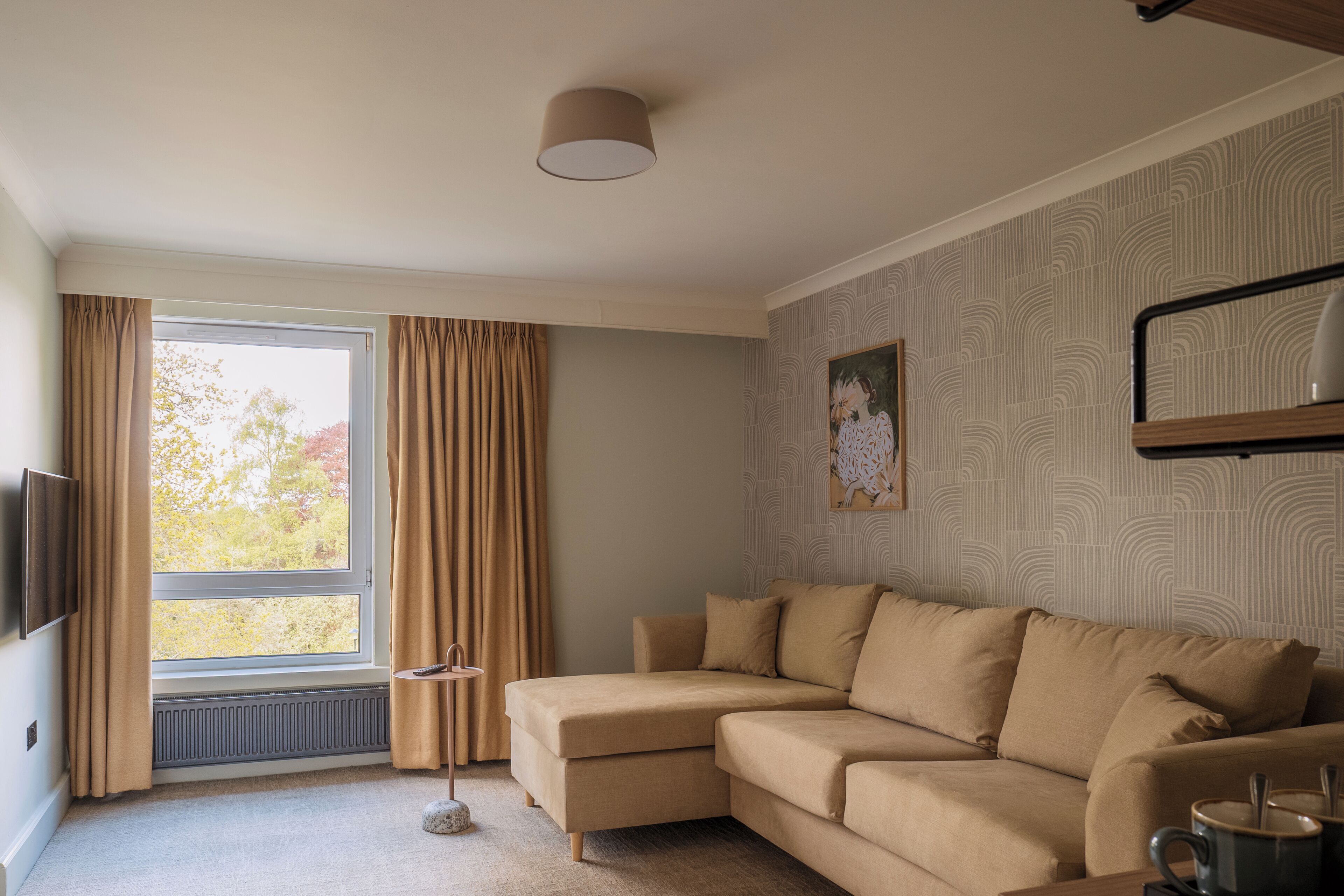 A modern living room with a sectional sofa, a flat-screen TV, a radiator, and a window with curtains.