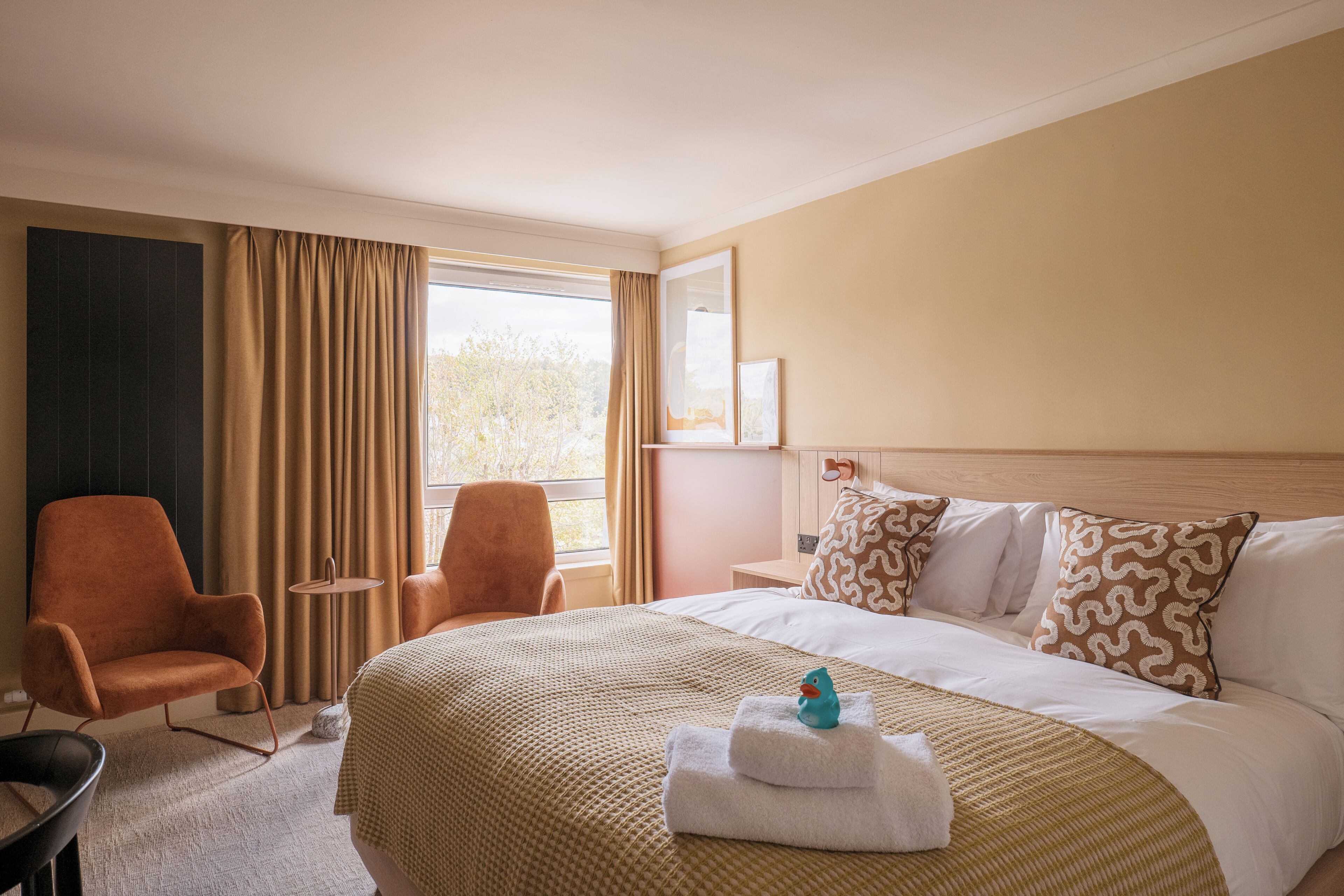 A hotel room with a bed, two chairs, a small table, and a window with curtains.
