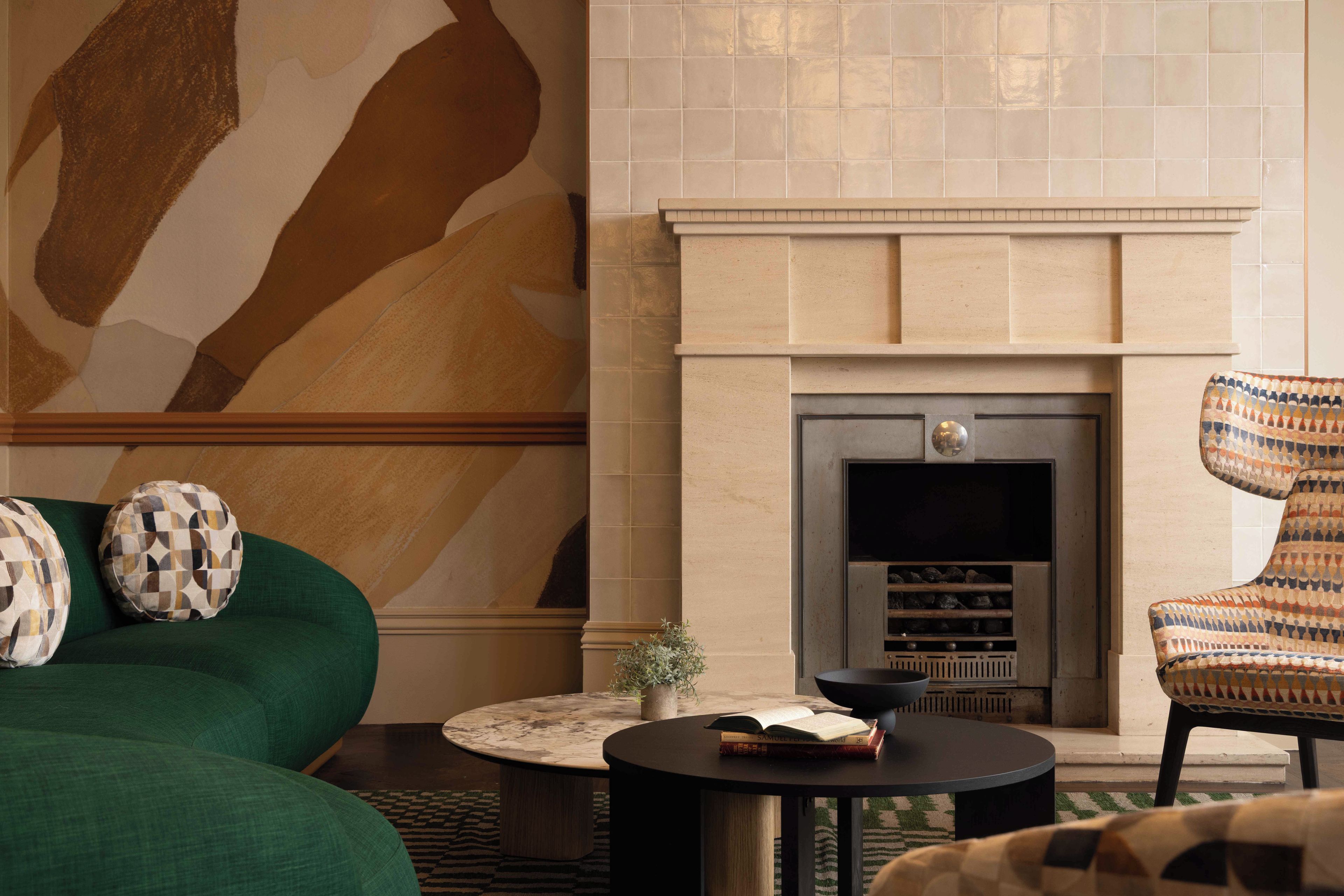 Una sala de estar con chimenea, sofá verde, cojines estampados y un sillón con diseño.