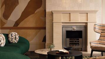Una sala de estar con chimenea, sofá verde, cojines estampados y un sillón con diseño.