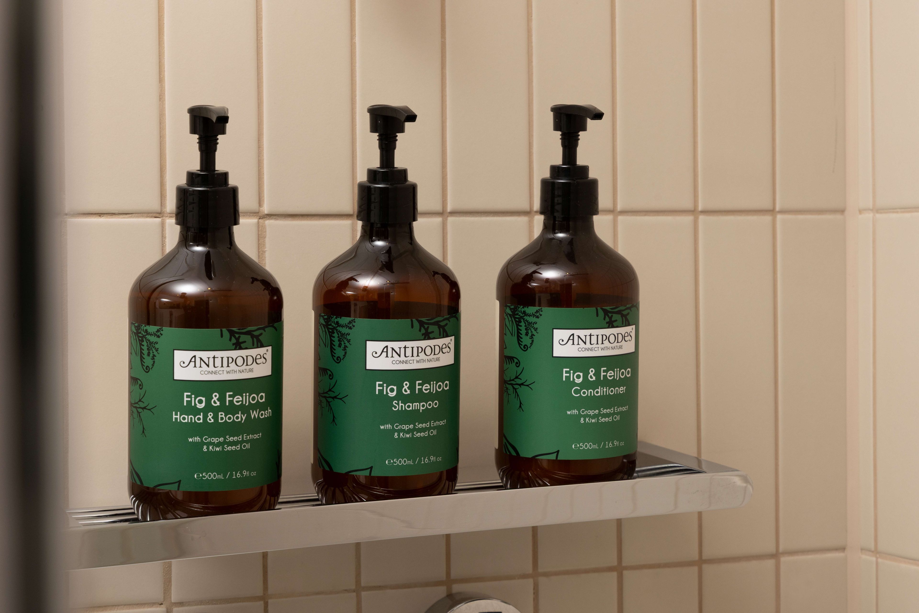 Three bottles of Antipodes Fig & Feijoa Hand & Body Wash on a white shelf against a tiled wall.