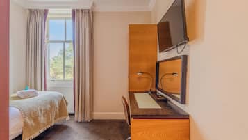 A hotel room with a bed, a desk with a computer, a TV, and a window with curtains.