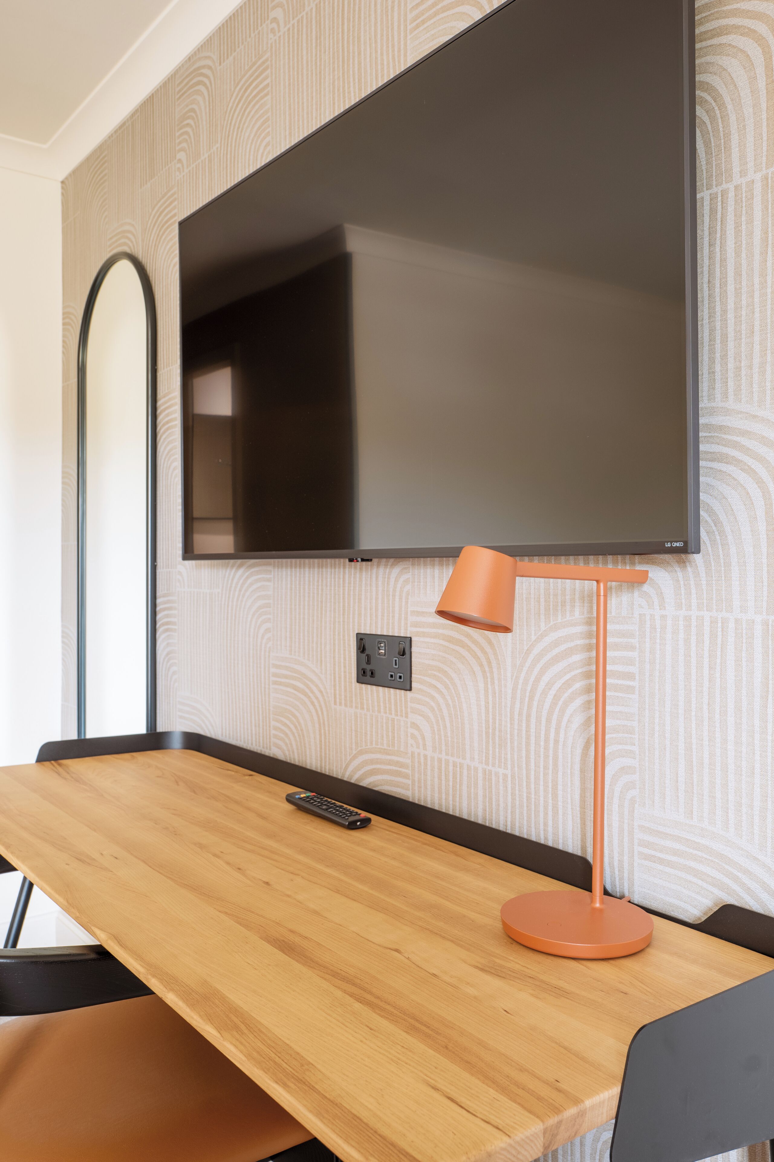 Ein modernes Zimmer mit einem wandmontierten Flachbildfernseher, einem Holztisch mit einer Fernbedienung und einer orangefarbenen Stehlampe.