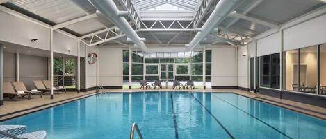 An indoor swimming pool with clear blue water, surrounded by lounge chairs and a glass ceiling.