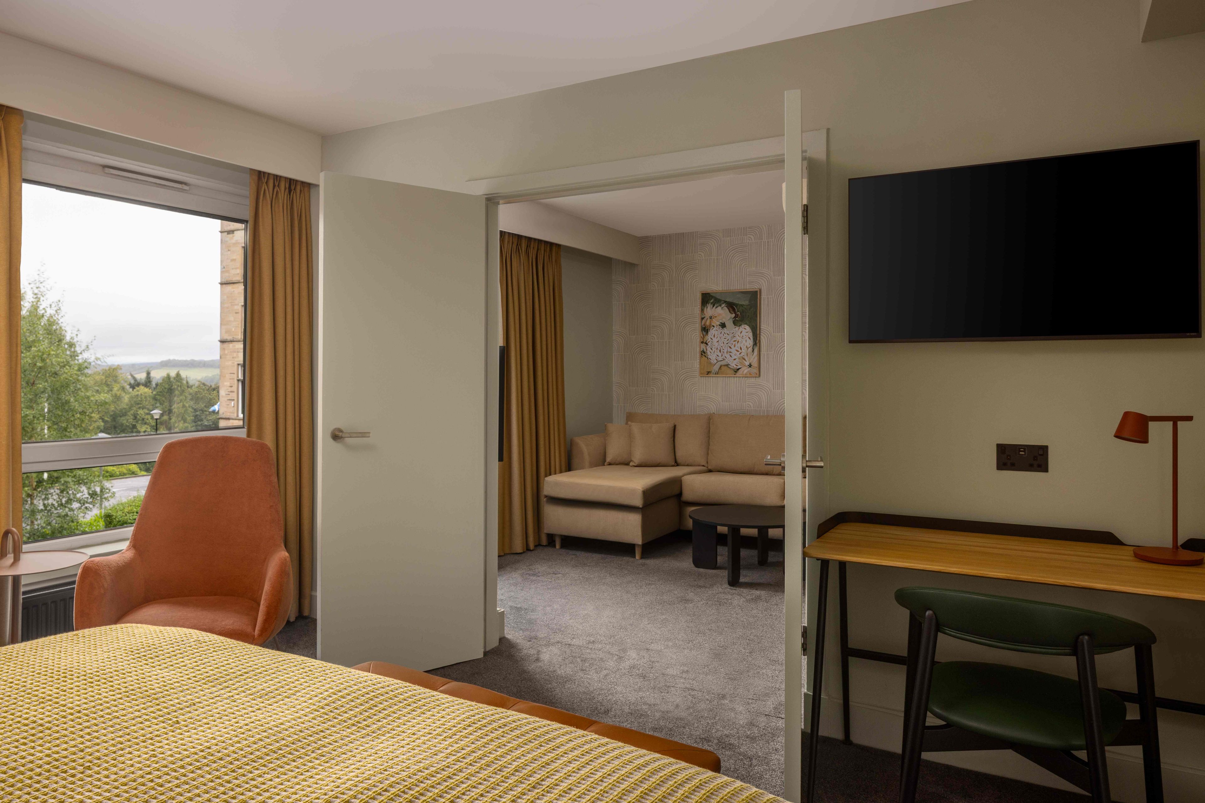 A hotel room with a bed, a desk, a chair, a sofa, and a TV.