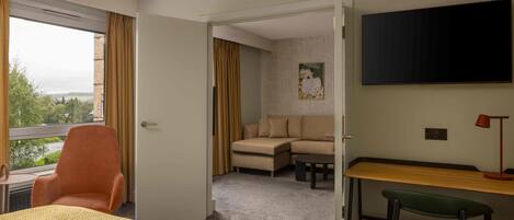 A hotel room with a bed, a desk, a chair, a sofa, and a TV.