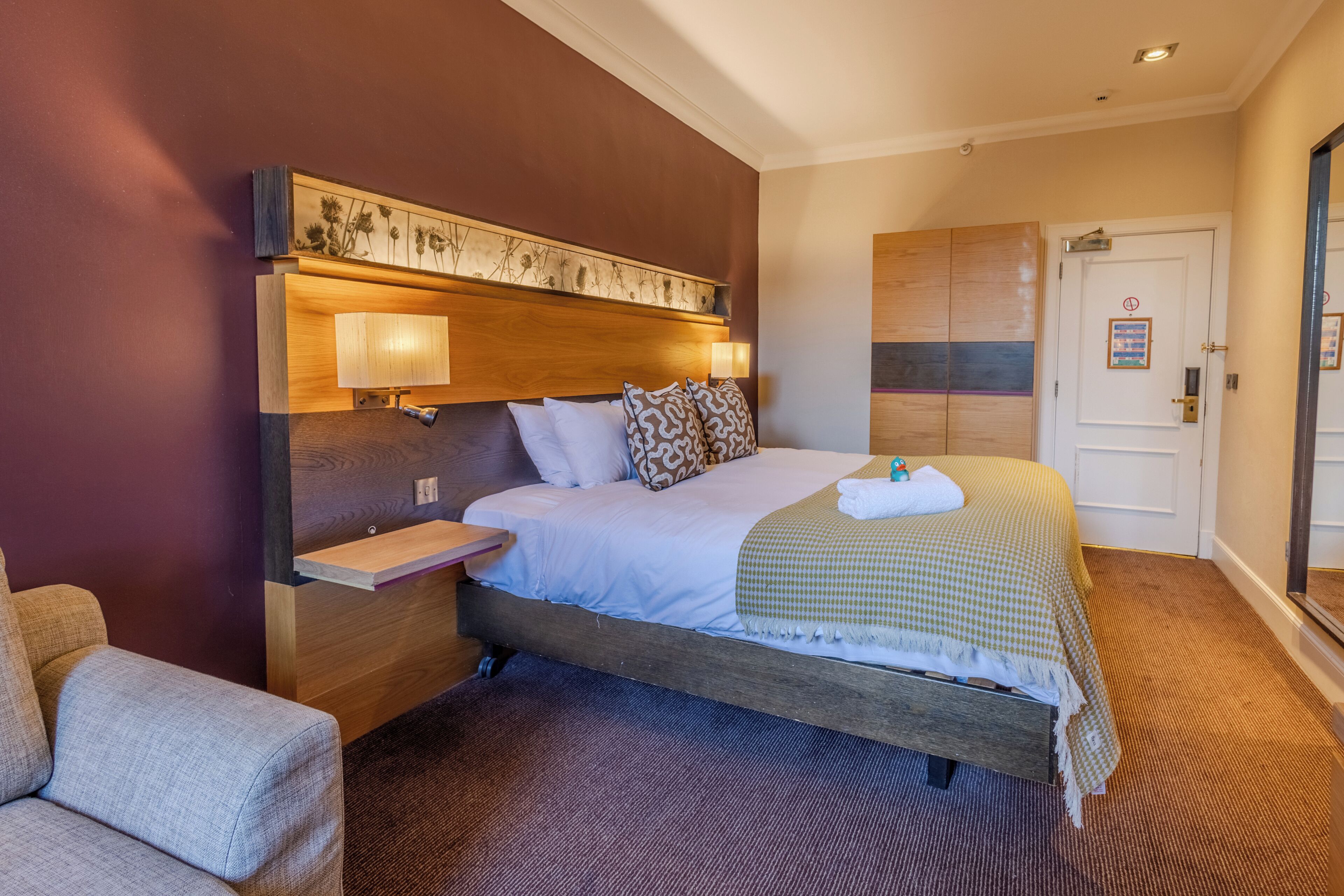 Una habitación de hotel con cama, mesita de noche, lámpara y una silla.