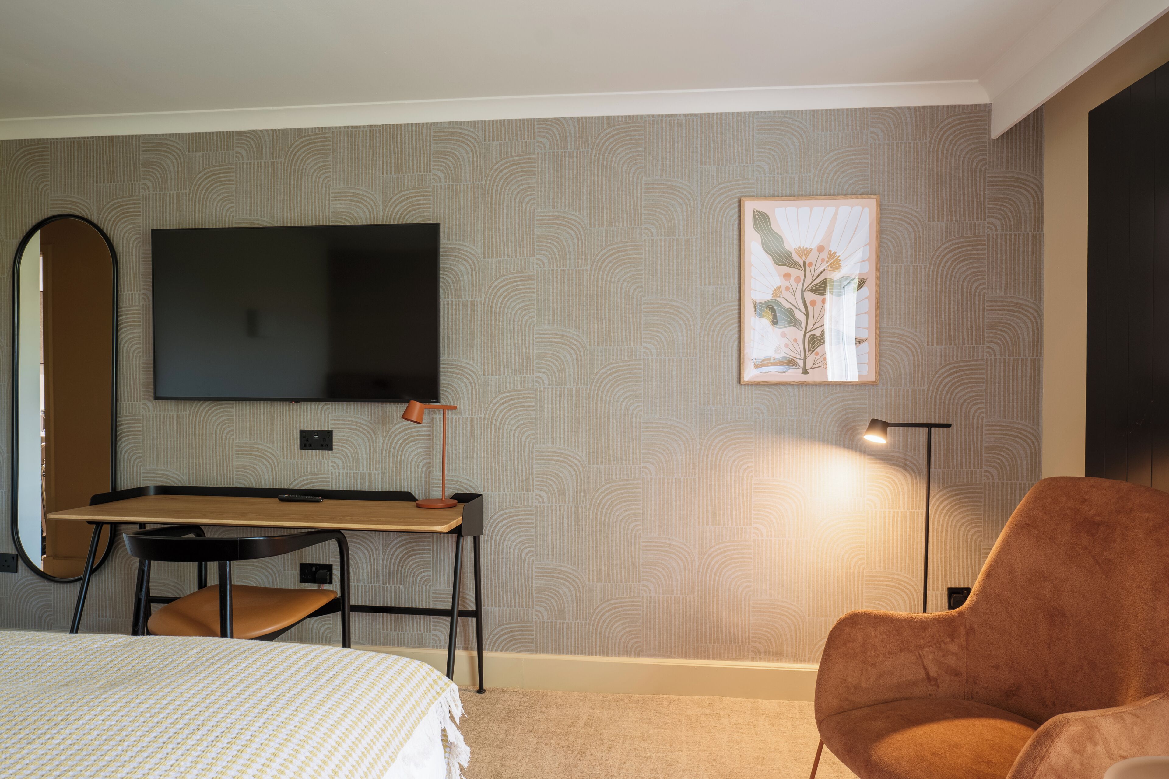Una habitación de hotel con cama, escritorio, silla, televisor, lámpara y un cuadro en la pared.