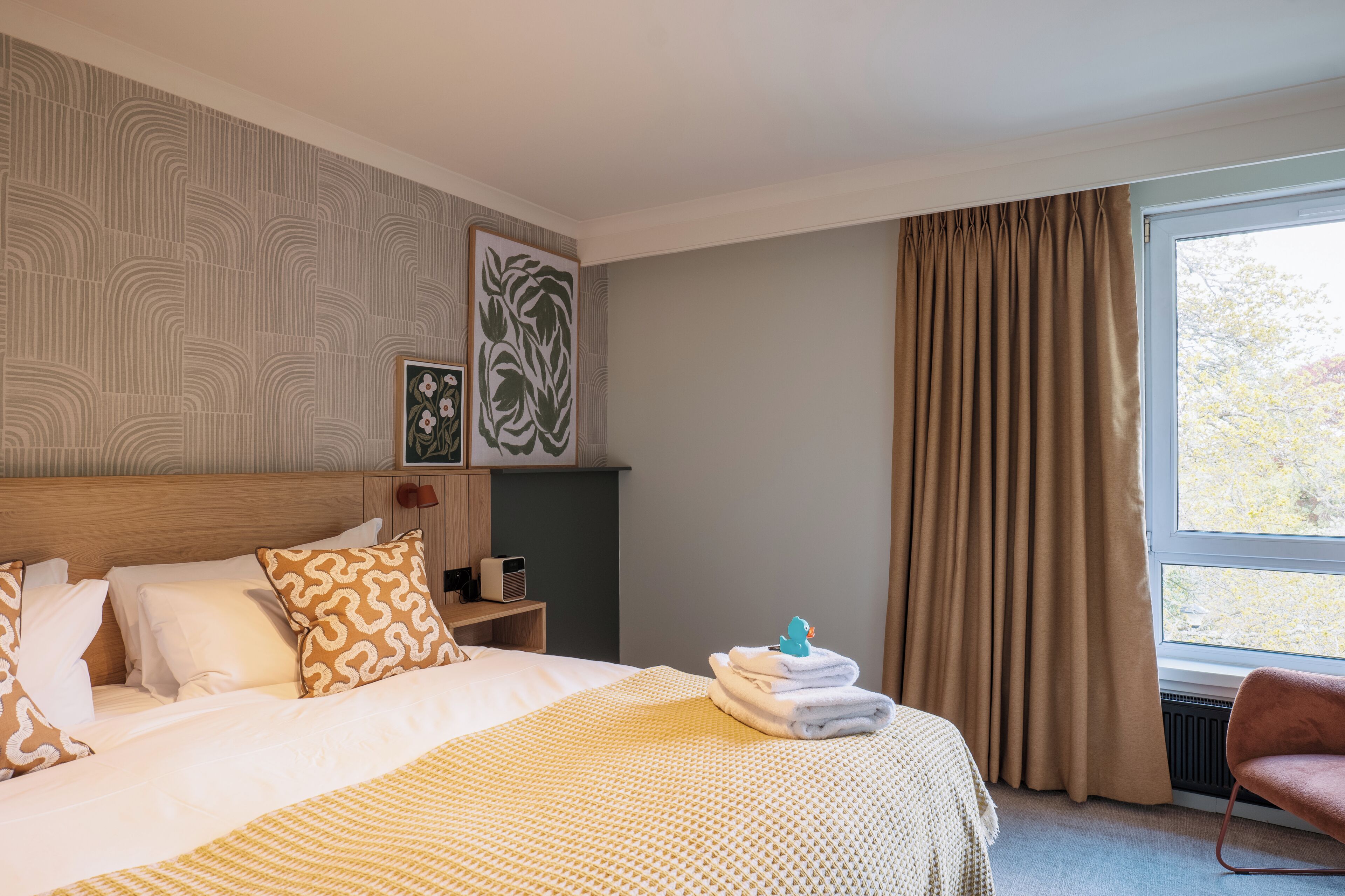 Une chambre d’hôtel avec un lit, une chaise, une fenêtre avec des rideaux et des œuvres d’art mural.