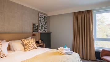 Habitación de hotel con cama, una silla, ventana con cortinas y decoración en la pared.