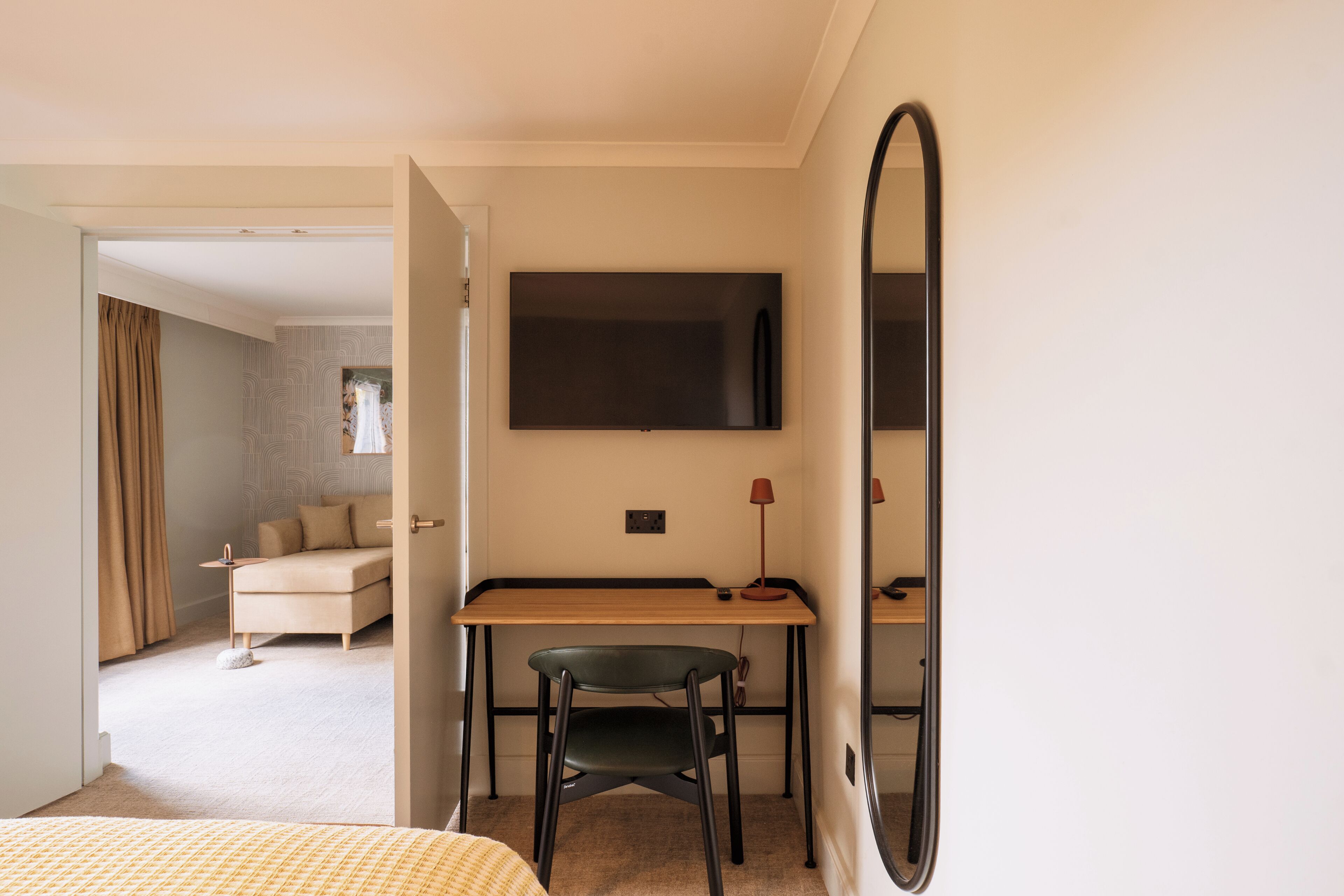 Un dormitorio con cama, escritorio, silla, televisor y espejo.