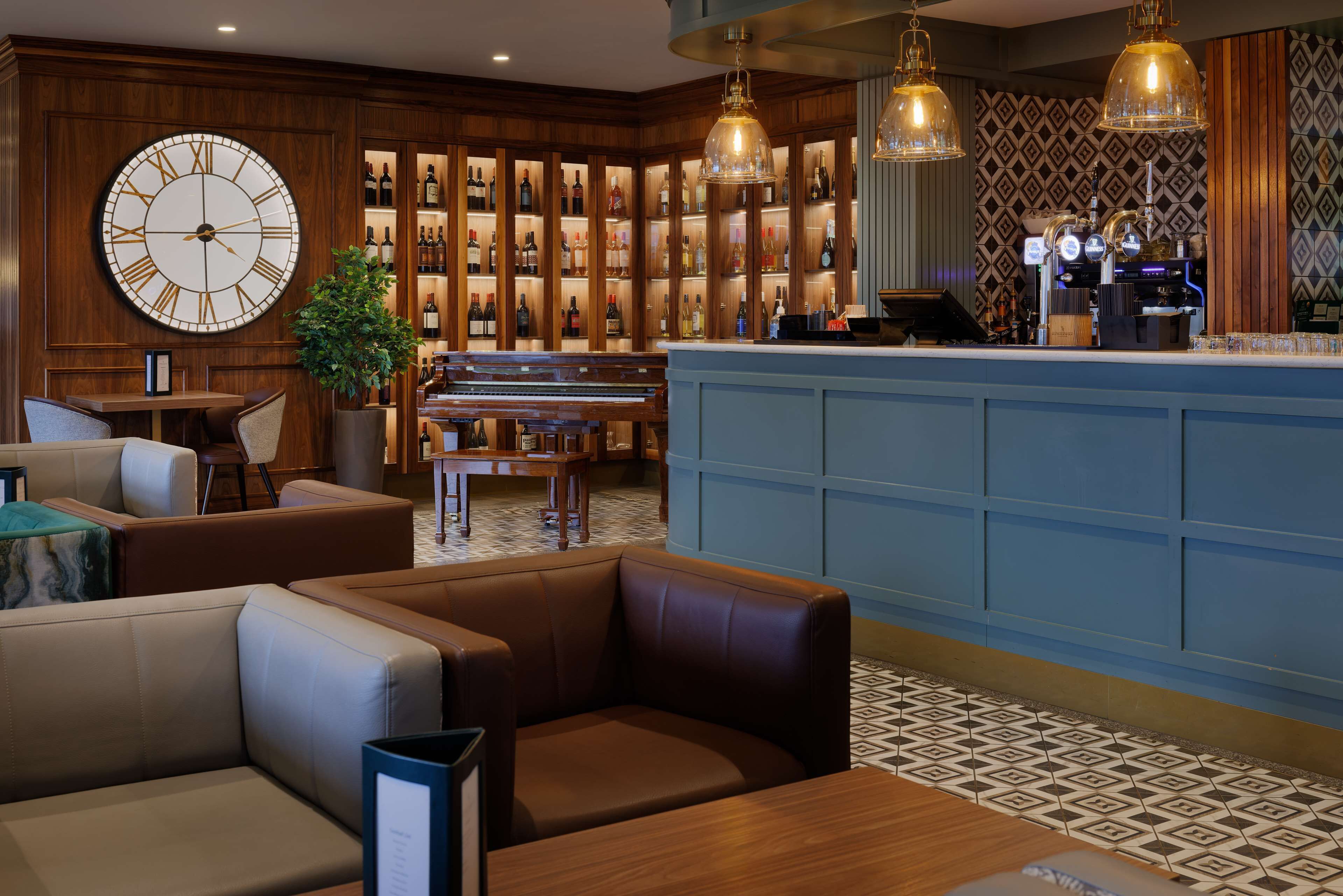 A bar area with a large clock, wooden shelves with bottles, and seating.