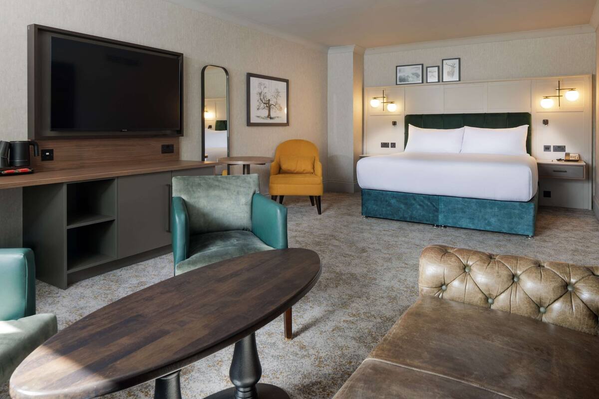 A hotel room with a bed, a TV, a sofa, a chair, a coffee table, and a desk.