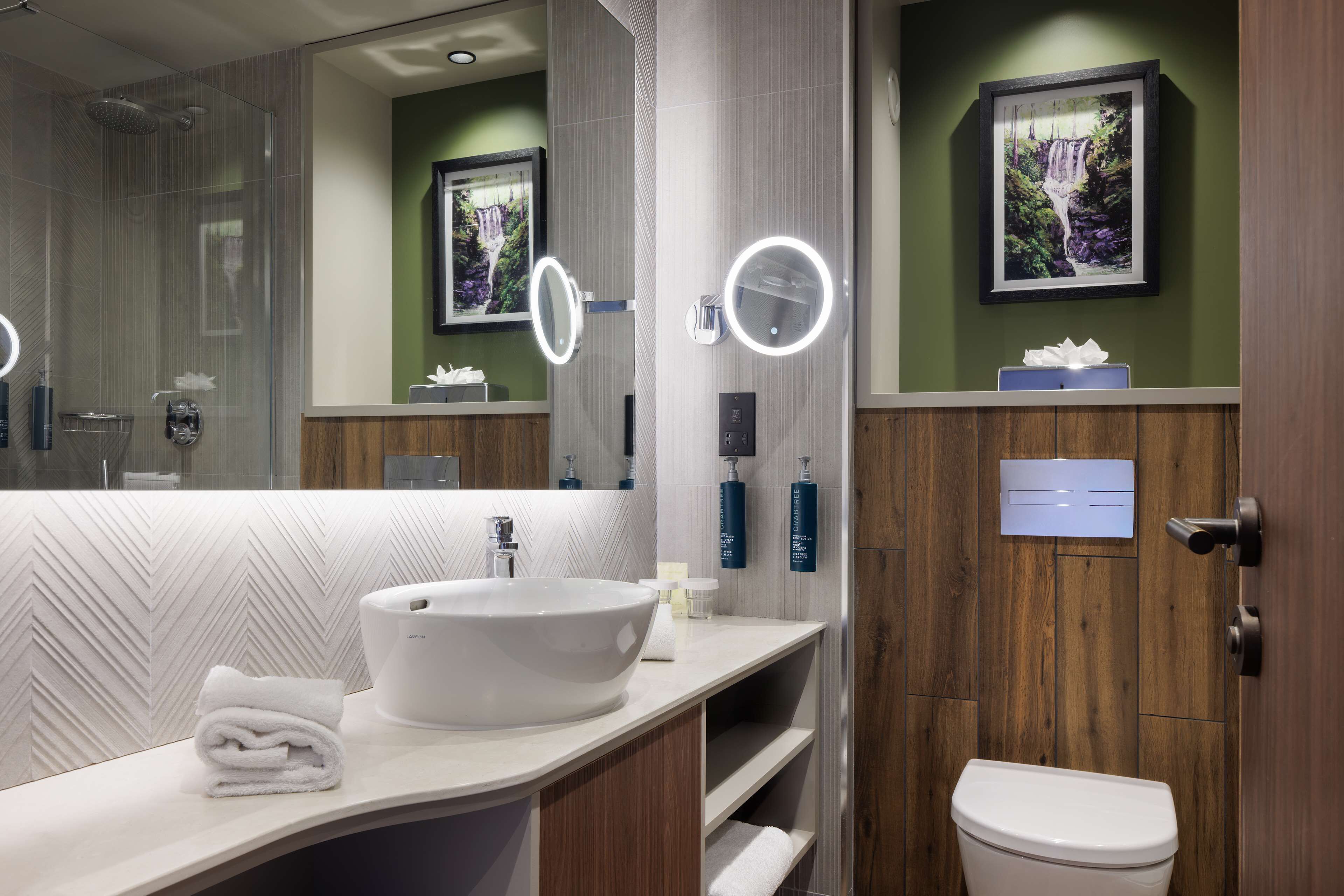 A modern bathroom with a large mirror, a white sink, and a toilet.