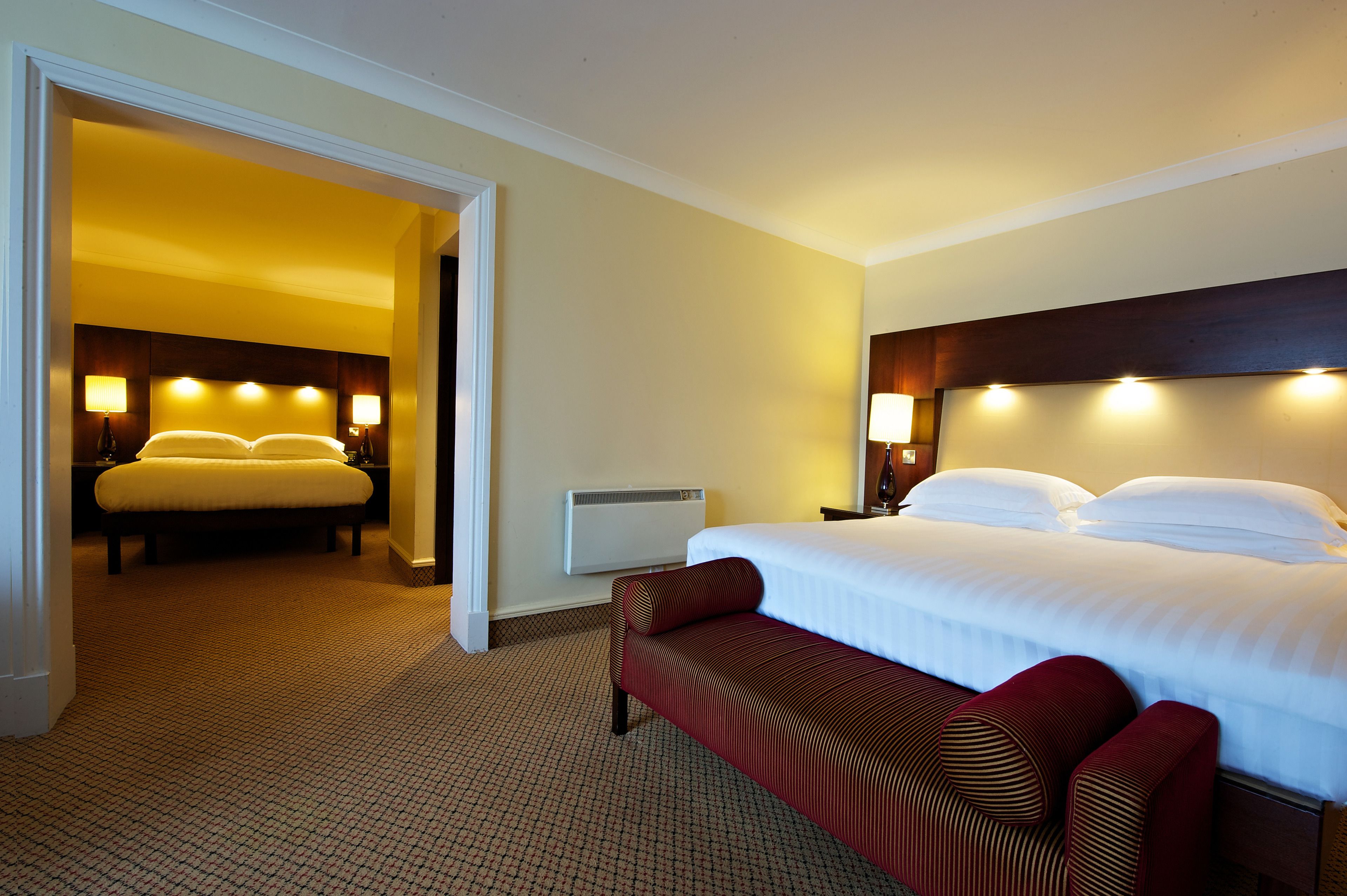A hotel room with a large bed, a bench, and two bedside lamps.