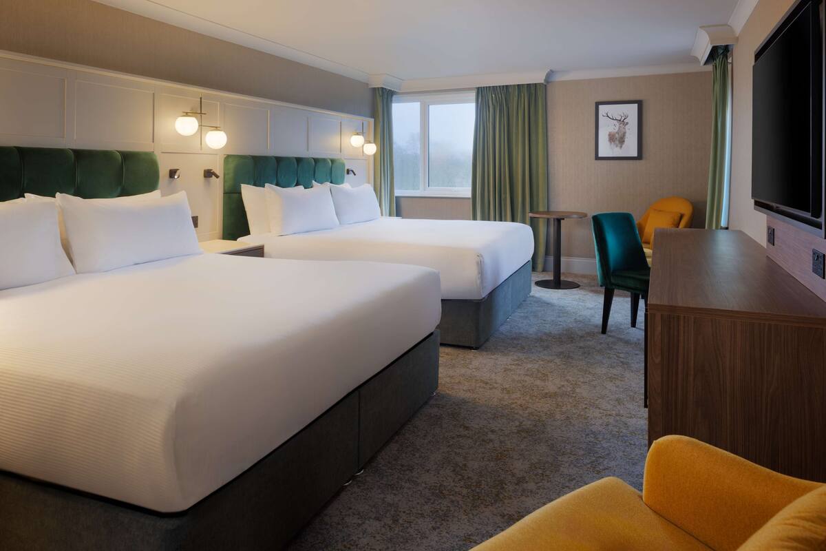 A hotel room with two beds, a desk, a TV, and a chair.