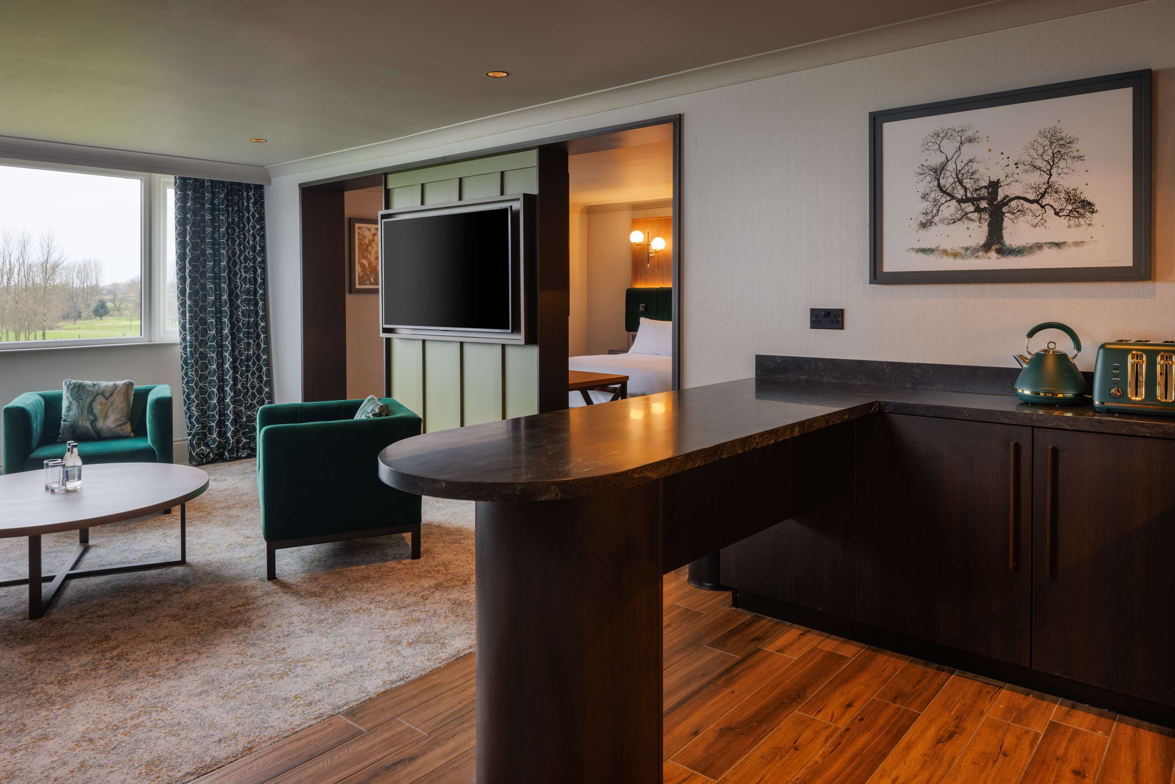 Una habitación de hotel moderna con un televisor de pantalla plana grande, una zona de comedor con bar y vistas al exterior.