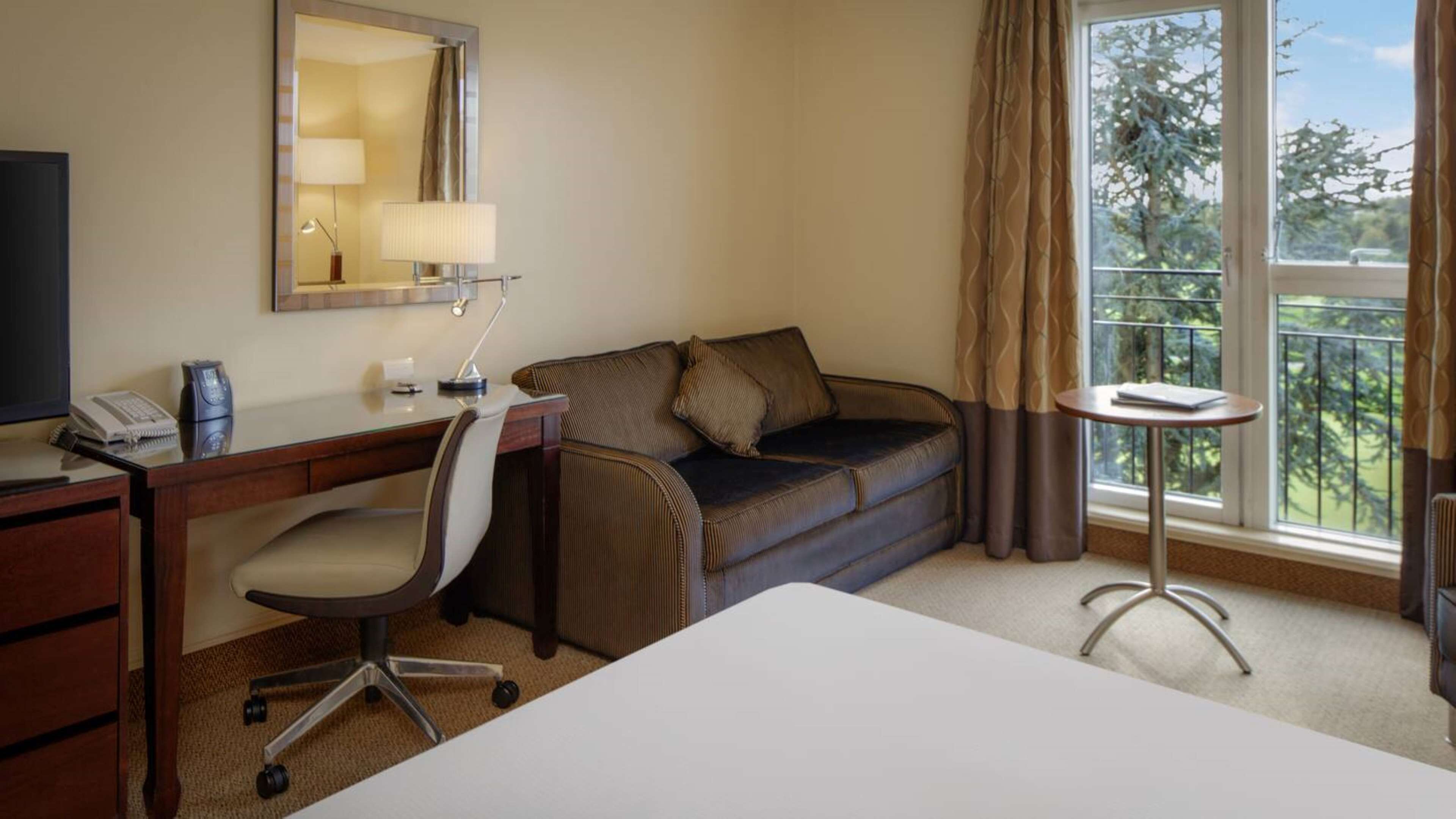 A hotel room with a desk, chair, sofa, and a small table by the window.