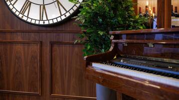 Un piano de cola, un reloj de pared grande y una planta en maceta en una sala con paneles de madera.