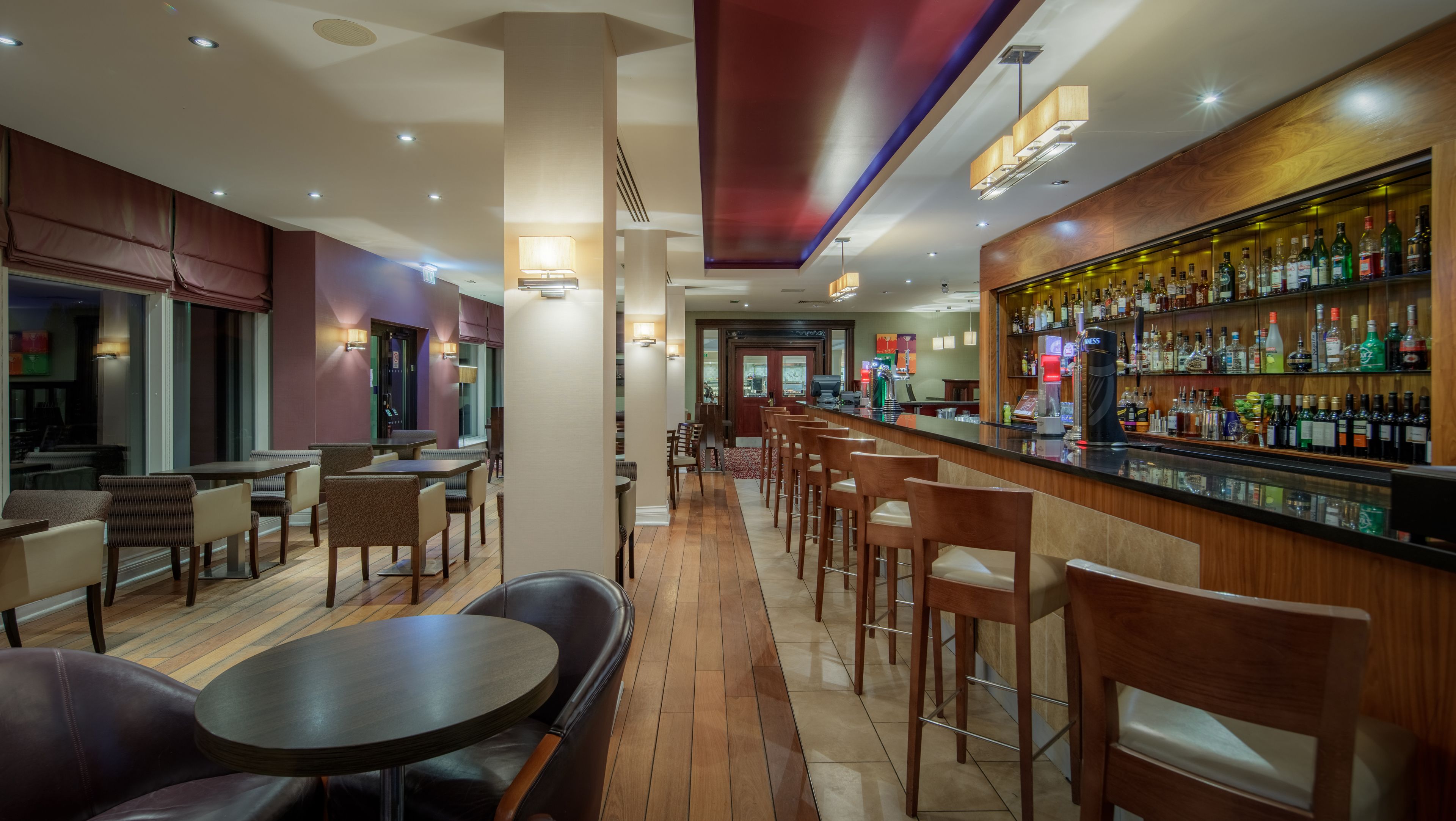 Una zona de bar con mobiliario de madera, una variedad de botellas de licores y un espacio de estar con mesas y sillas.
