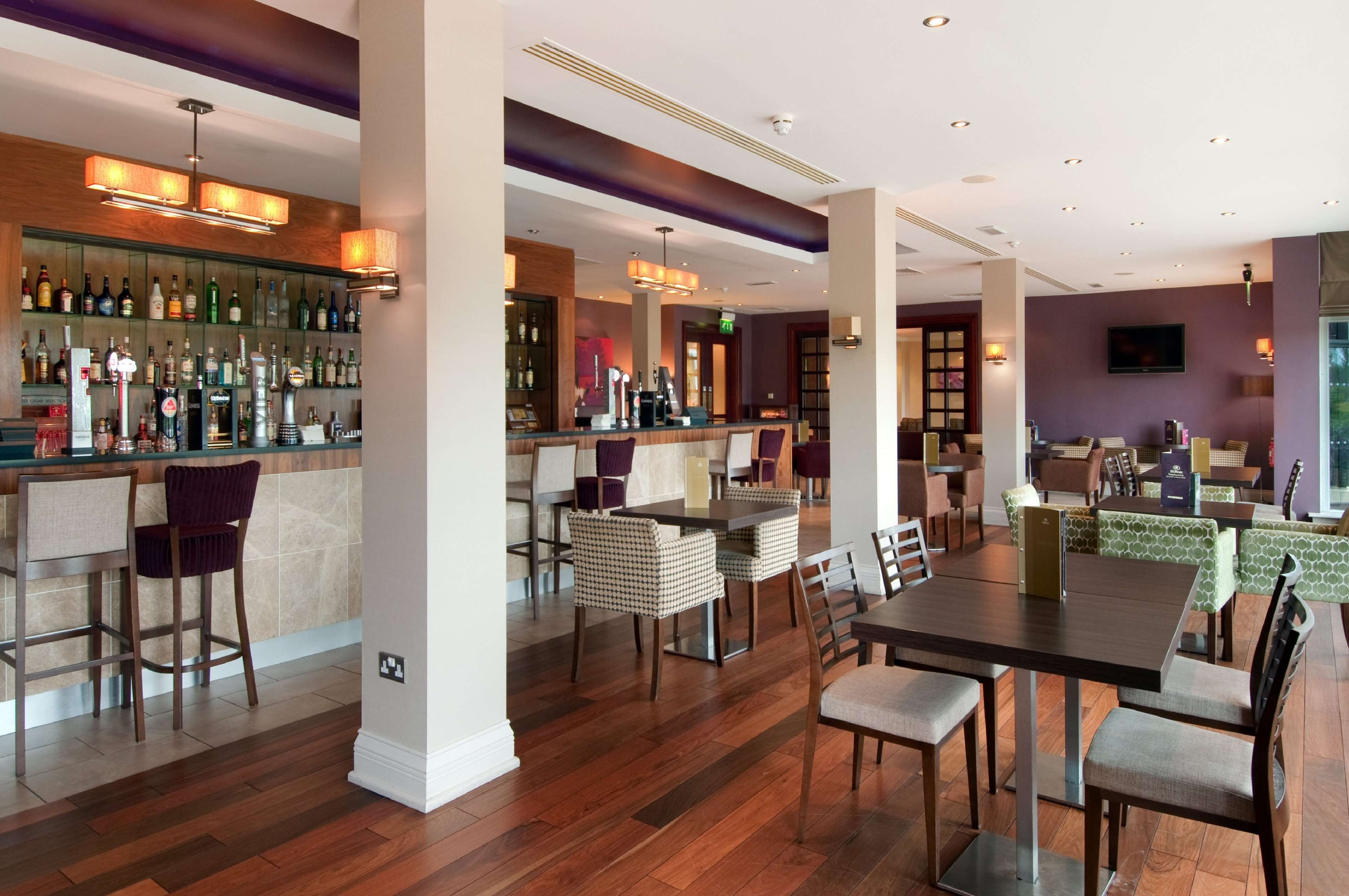 A bar area with a long counter and multiple stools, a dining area with a table and chairs, and a seating area with sofas and chairs.