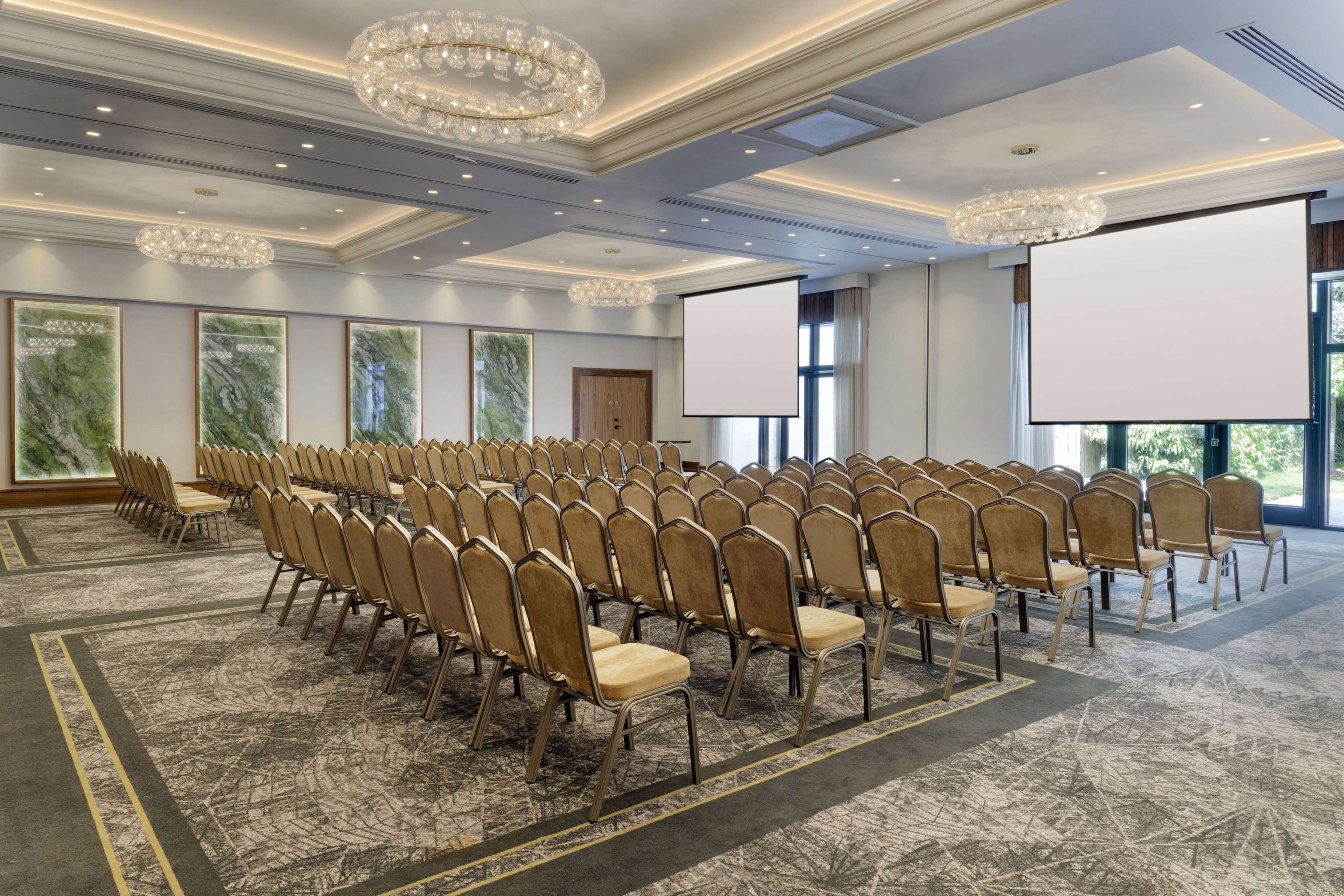 Ein Konferenzraum mit Stuhlreihen, einer großen Leinwand und Kristalllüstern.