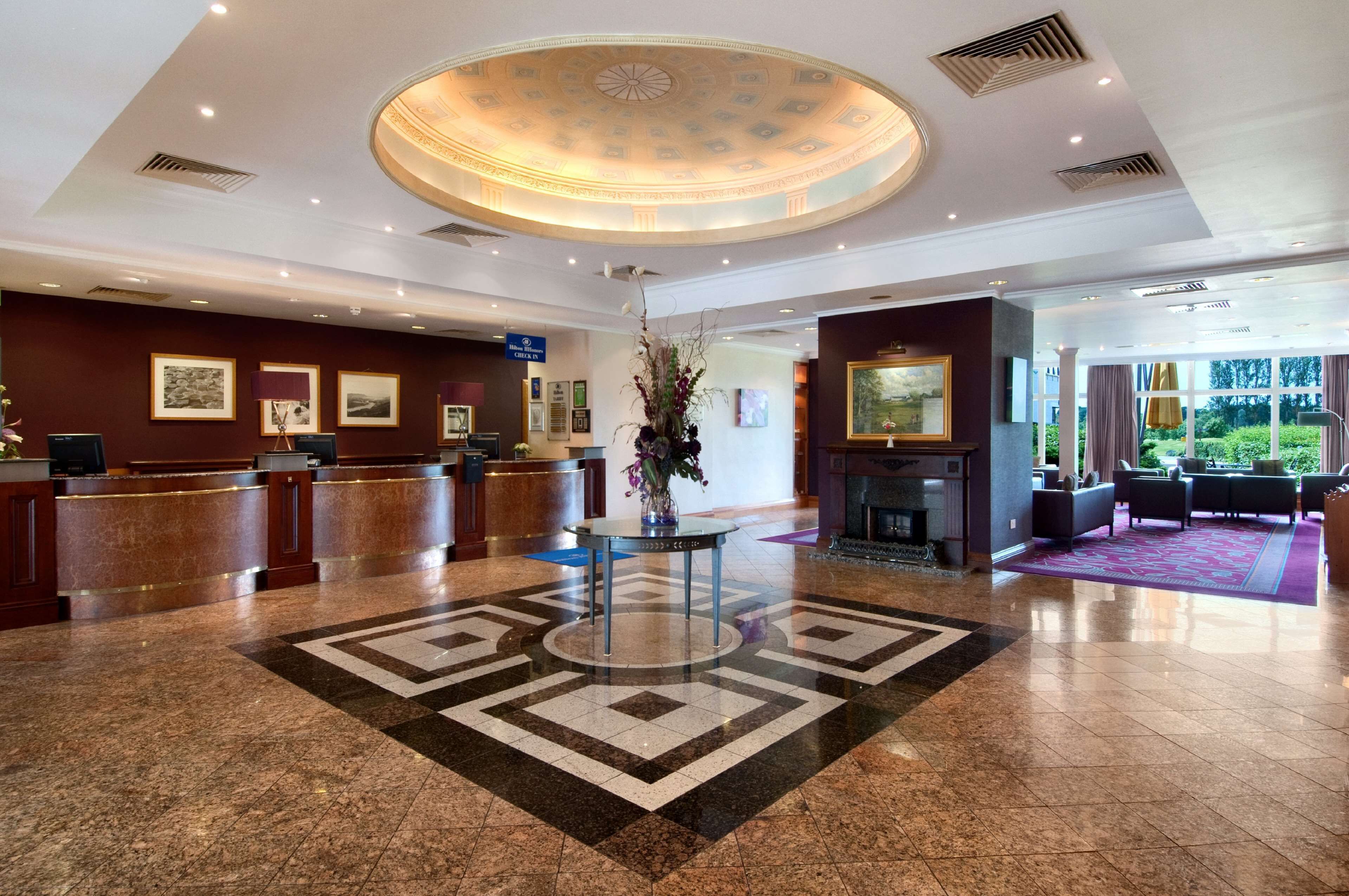 Vestíbulo de hotel con mostrador de recepción, obra de arte enmarcadas, techo decorativo y zona de estar con alfombra estampada.