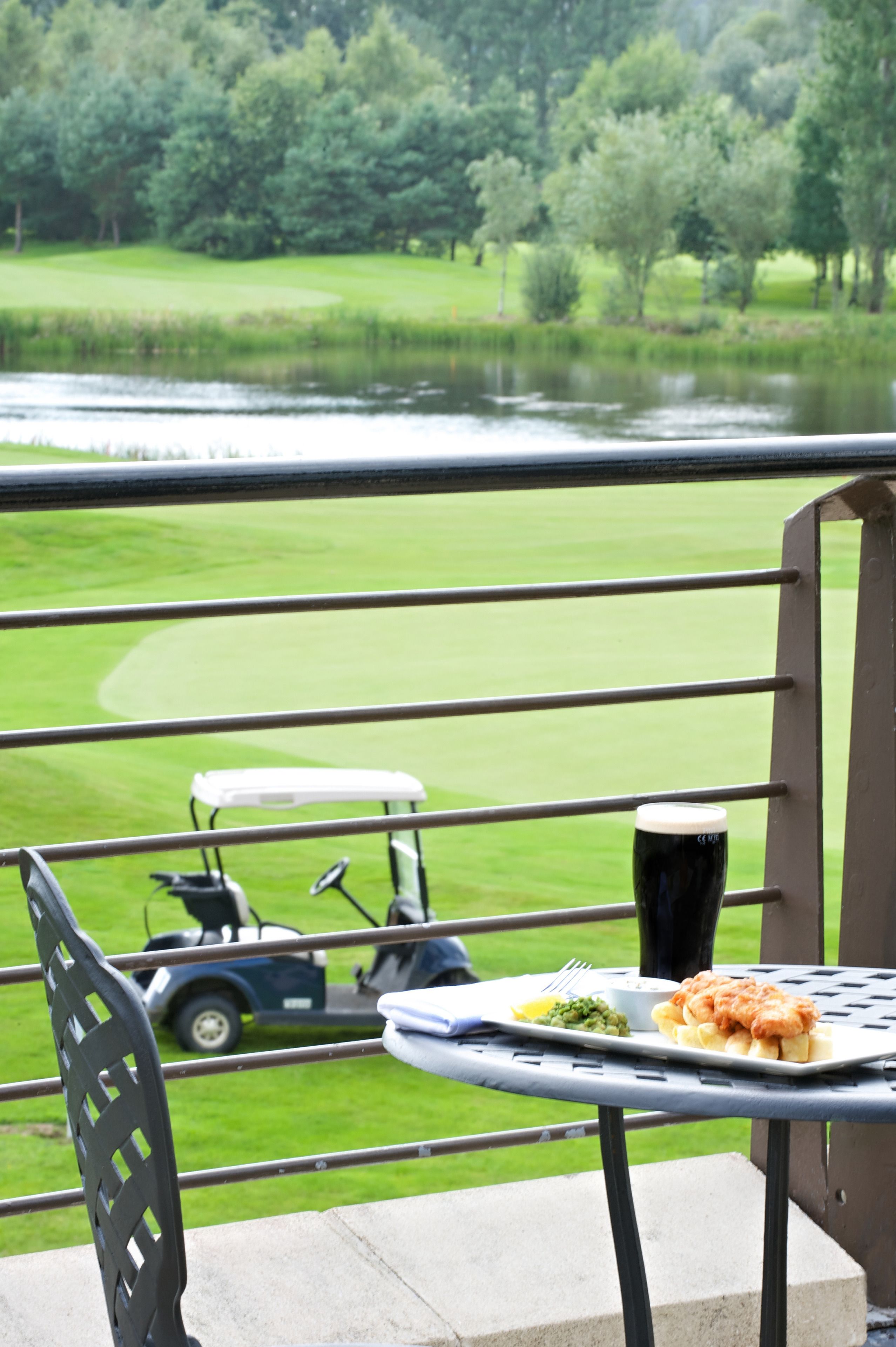 Una mesa de comedor con comida y una jarra de cerveza, con vista a un campo de golf y una masa de agua.