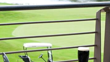 Una mesa de comedor con comida y una jarra de cerveza, con vista a un campo de golf y una masa de agua.
