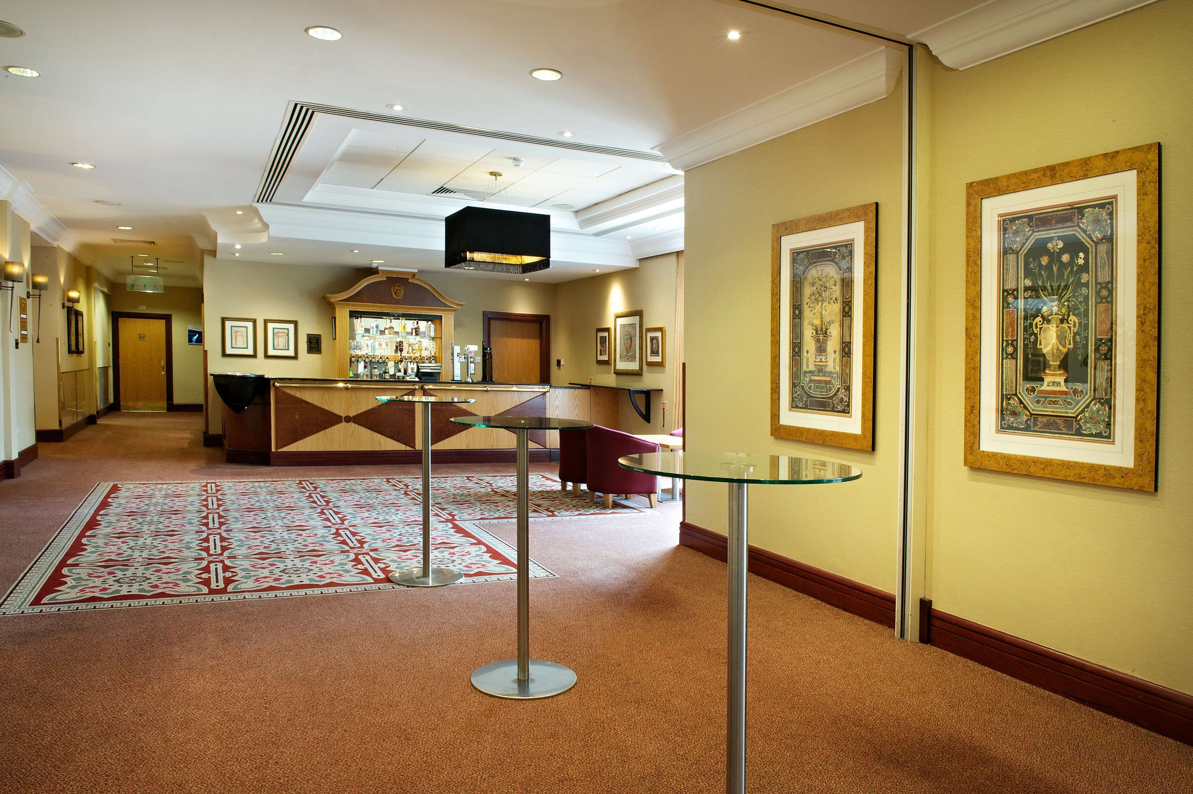 Una hall d'albergo con una reception, un tavolino in vetro, un tappeto decorato e quadri appesi alle pareti.